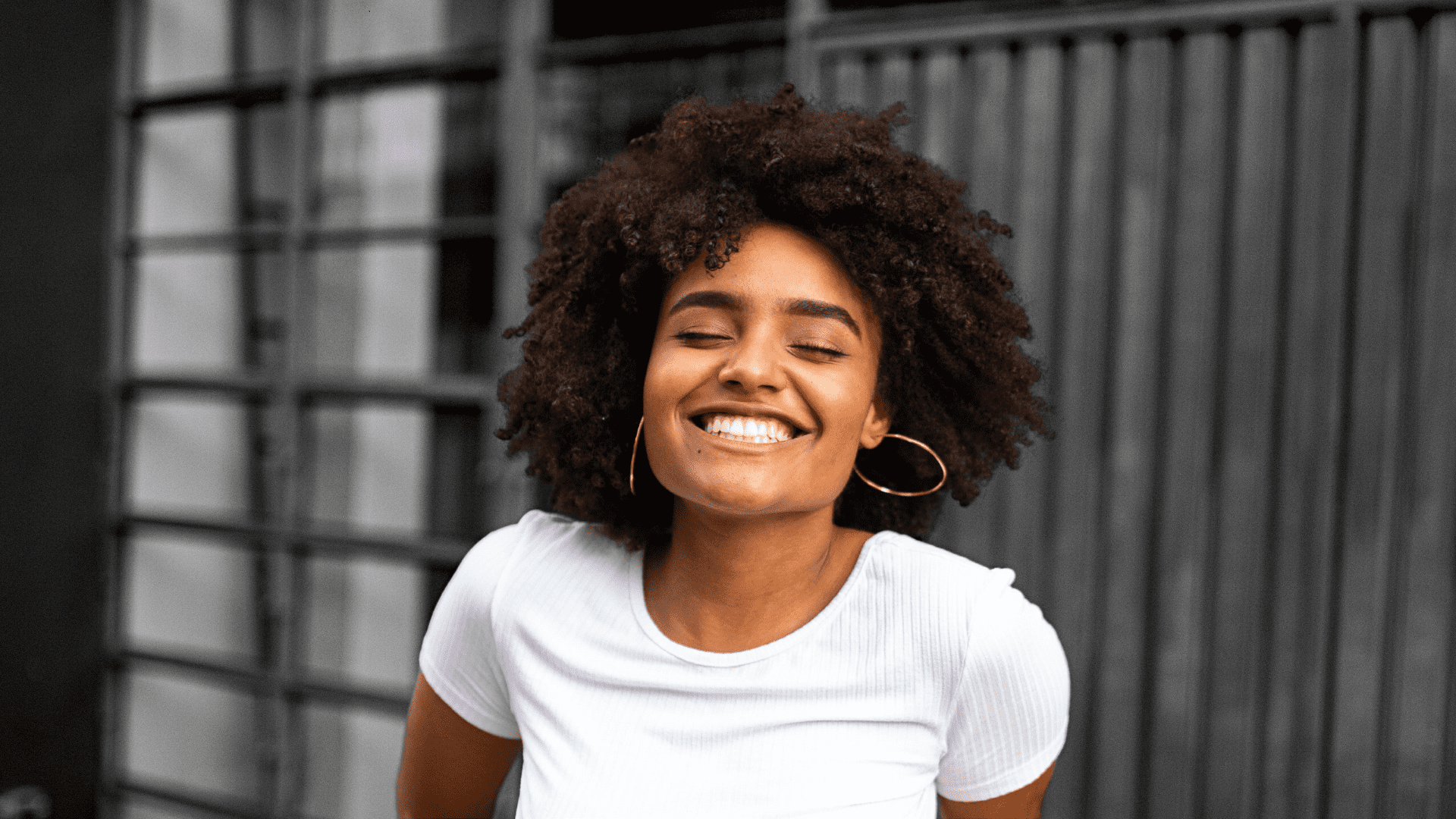 Smiling woman with curly hair and gold hoops.