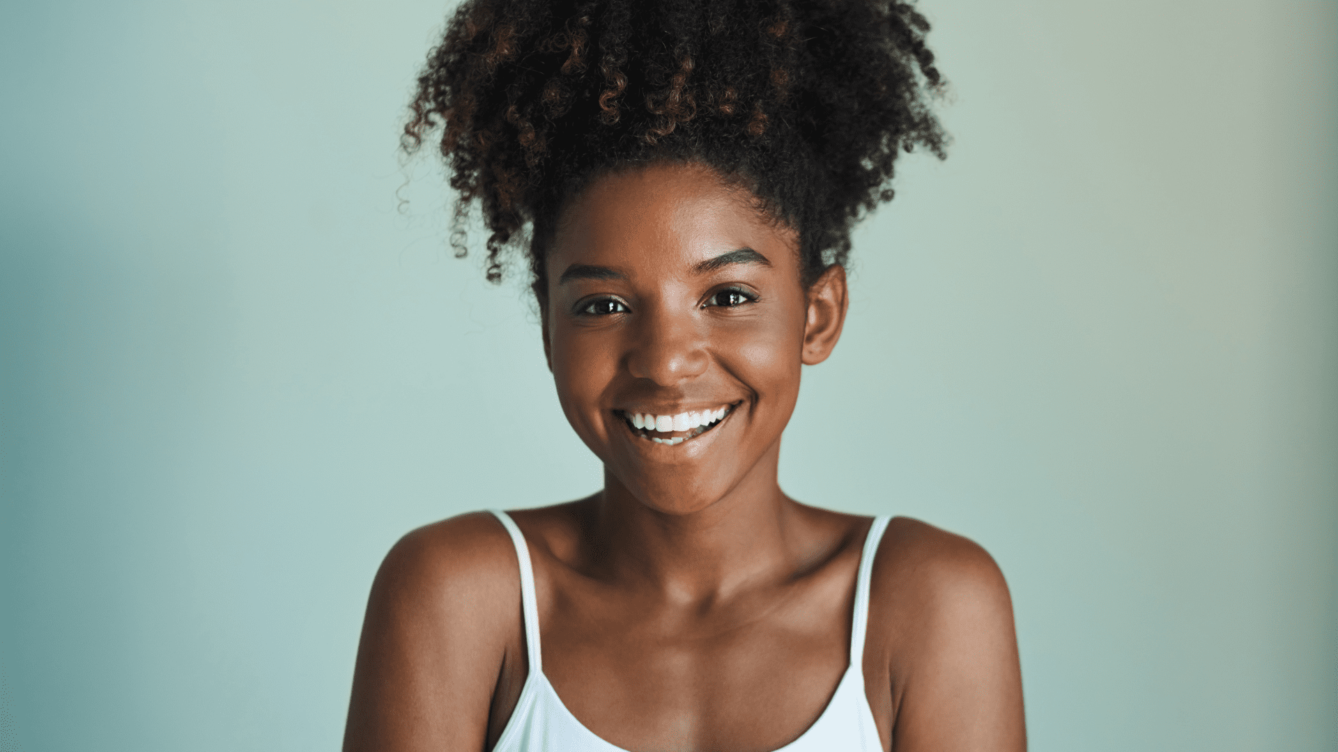 Smiling woman with curly hair in a white tank top.